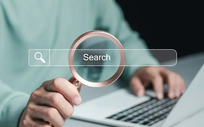 Person holding magnifying glass over laptop.
